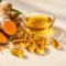 Fresh turmeric root beside amber NovaSOL curcumin softgels and a dish of clear golden liquid